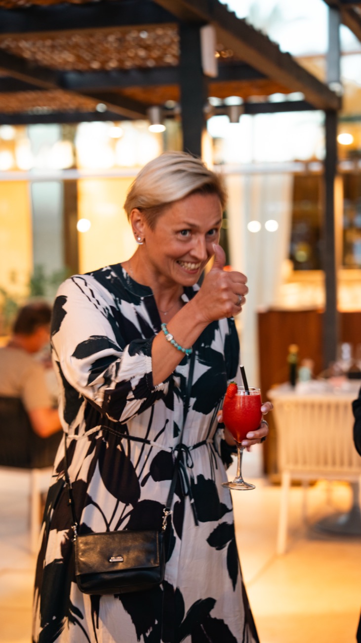 A woman smiling and giving a thumbs up with a drink in hand