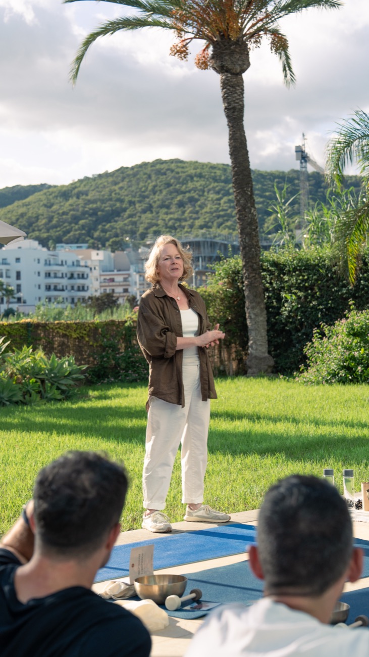 A woman leading an outdoor morning session under palm trees